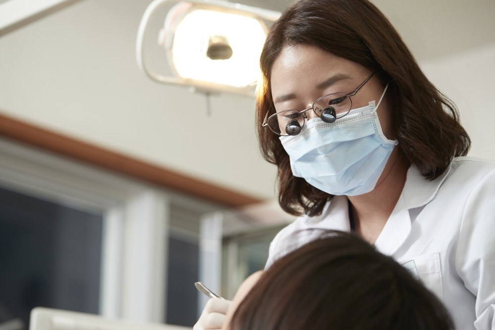 김해 뉴욕치과병원 권수정 원장이 확대경을 쓰고 치과 체어에서 환자의 치아를 살펴보는 모습