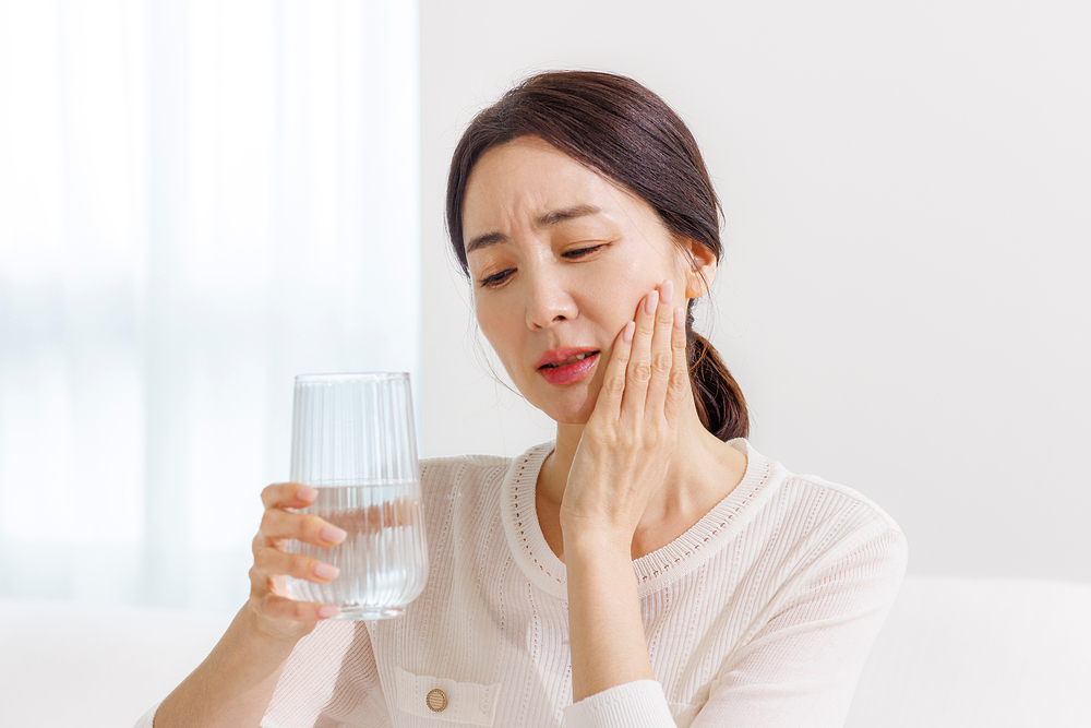찬물을 마신 뒤 치아가 시려 턱을 감싸고 있는 중년 여성